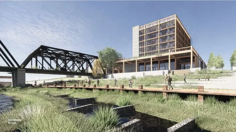 A modern building with large windows sits near a grassy area. People walk along a wooden path adjacent to a black metal bridge. Text reads: “Cori Medley, M.Arch.”