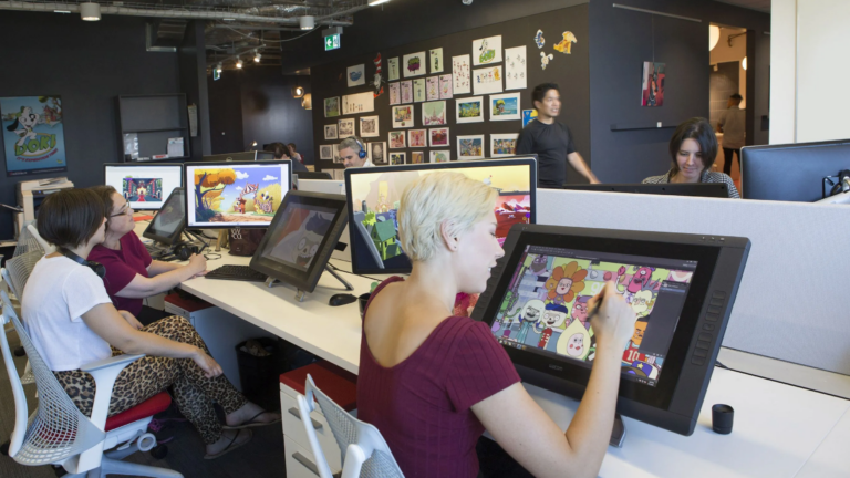 People working on digital drawing tablets in a modern animation studio with art displayed on walls.