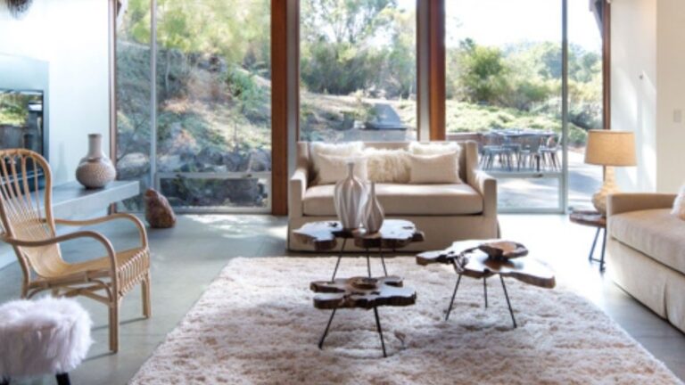 Living room with neutral furniture and large glass windows showing outdoor greenery.