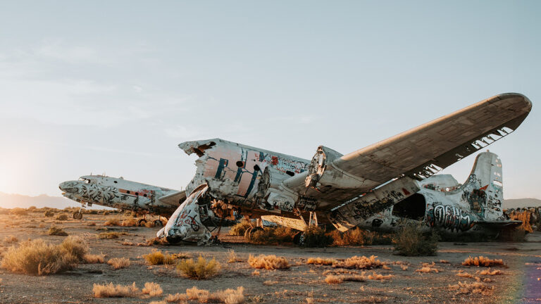 Dilapidated, graffiti-covered planes in a desert at sunset.