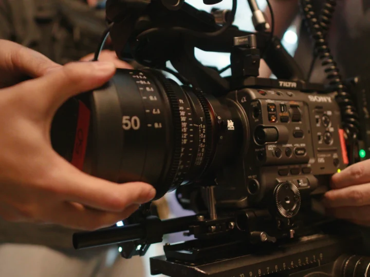 Close-up of hands adjusting a professional Sony video camera with a 50mm lens during a film production setup.