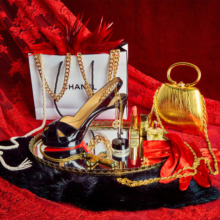 Black high-heeled shoes, jewelry, perfumes, lipstick, and a gold clutch on red lace fabric.