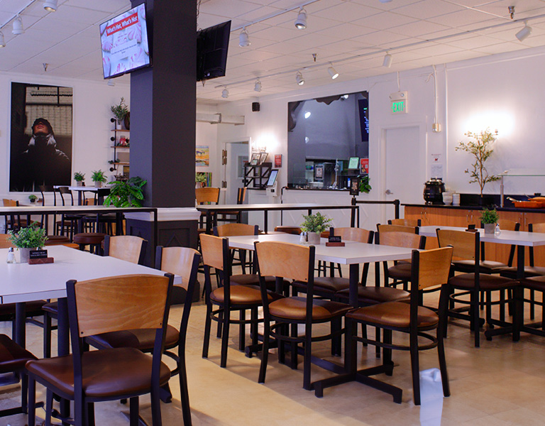 Empty dining area with tables, chairs, potted plants, and a service counter.