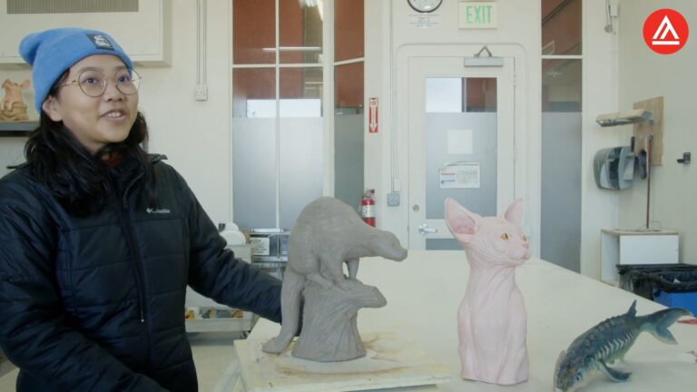 A woman in a black jacket and blue beanie stands next to animal sculptures on a table.