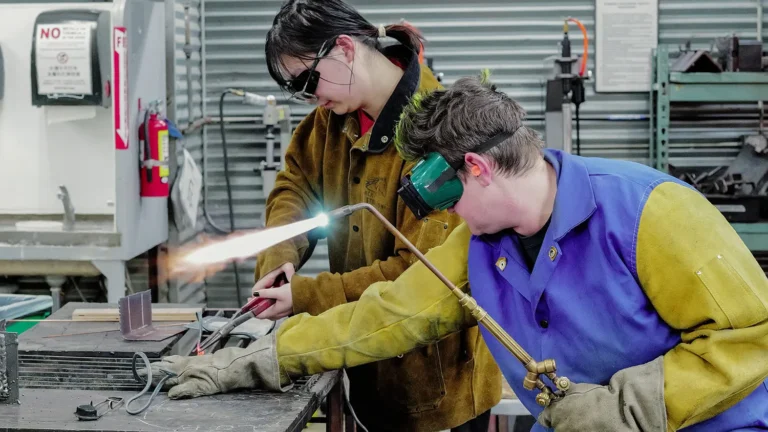 Two workers in protective gear welding metal in a workshop.