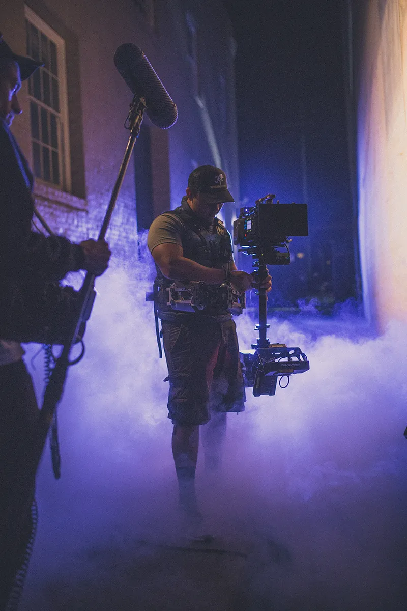 Crew member operating camera in a foggy, dimly lit setting during filming.