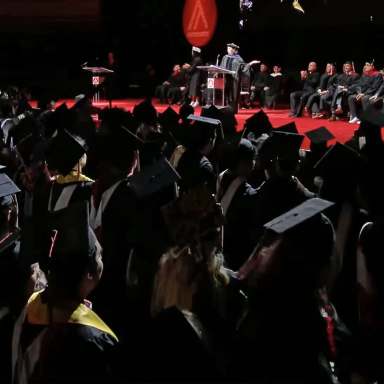 Graduates in caps and gowns attending a commencement ceremony on stage.