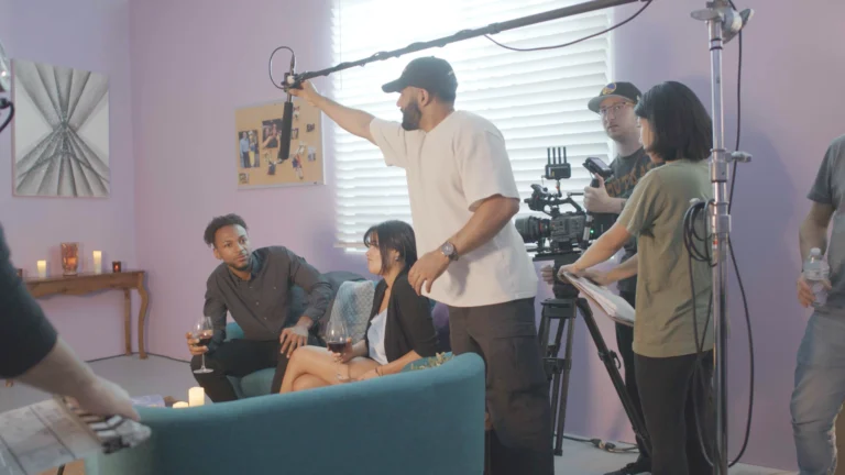People filming a scene in a room with purple walls and candles on a table.