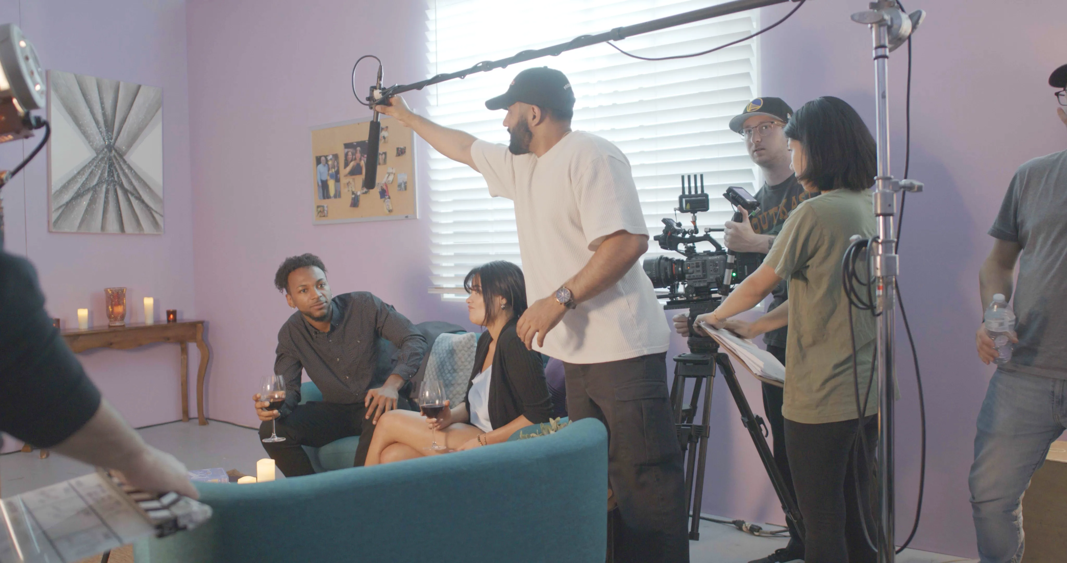 People filming a scene in a room with purple walls and candles on a table.