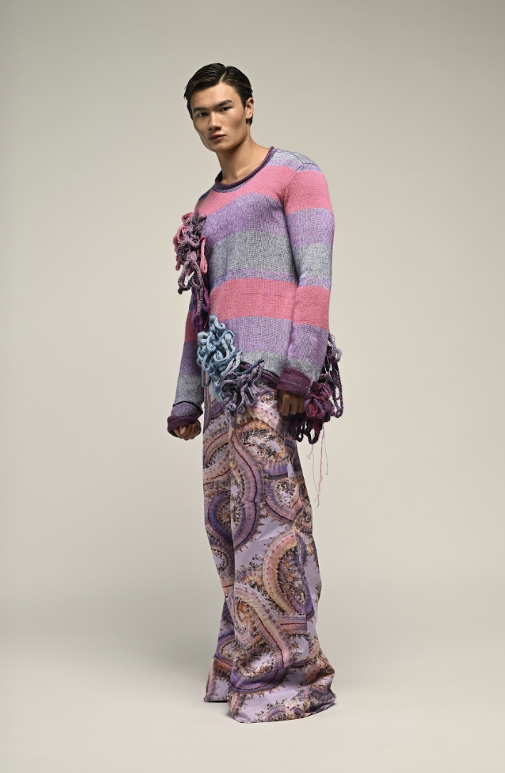 Person wearing a colorful striped sweater with 3D yarn decorations and patterned wide-leg pants.
