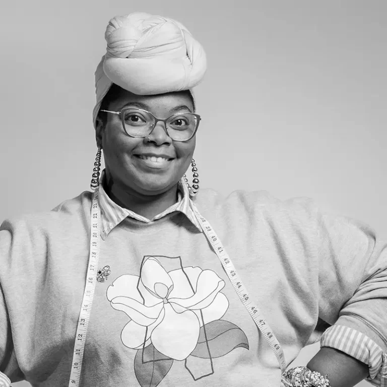 smiling woman with glasses, headwrap, and measuring tape around her neck