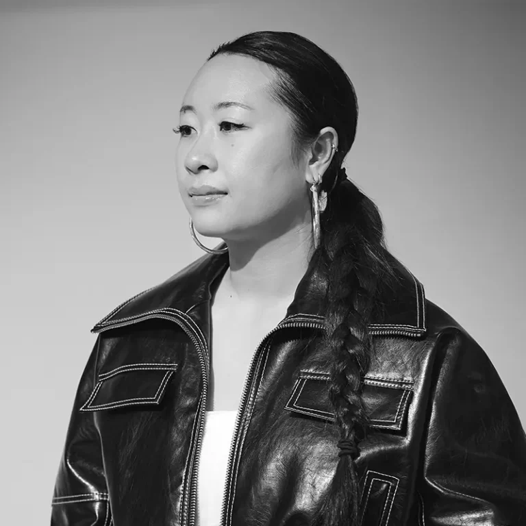 Woman with braided hair wearing a leather jacket and hoop earrings.