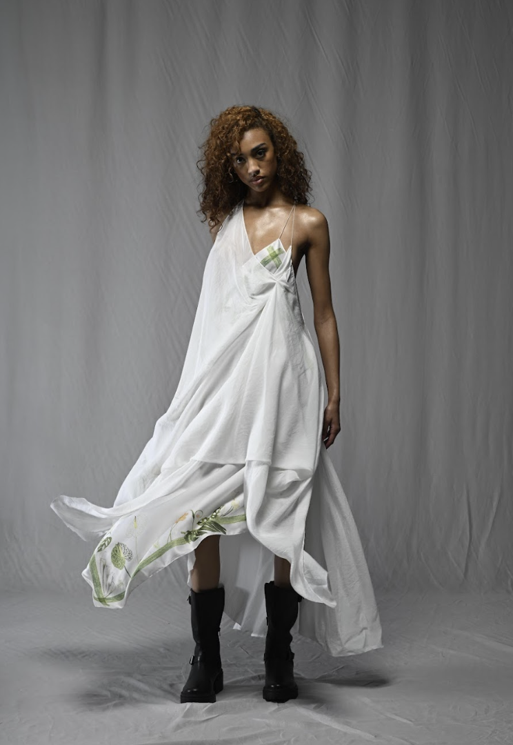 Woman in a flowing white dress and black boots standing indoors.