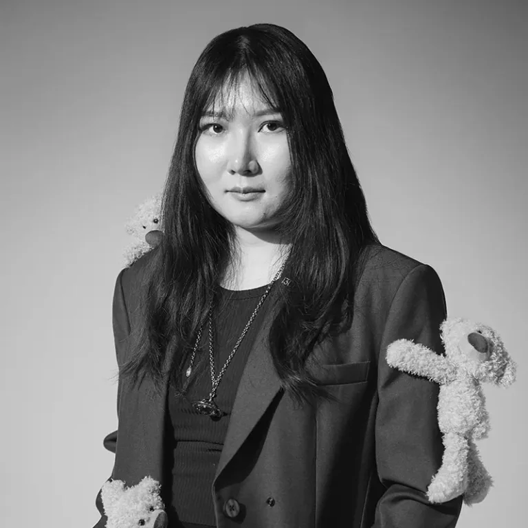 Woman with long dark hair wearing a blazer with teddy bear accessories on shoulders.