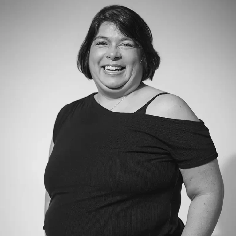 A woman smiling, wearing a black off-the-shoulder top with spaghetti straps.