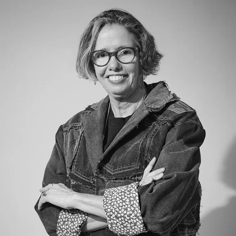 Woman with glasses smiling and crossing arms, wearing a denim jacket.