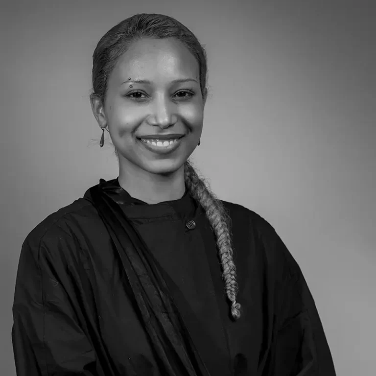 Smiling woman in judicial robe with braid and earrings against plain background.