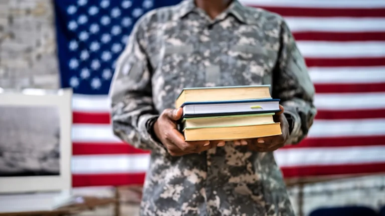 Person in military camouflage holding books against an American flag, Military Credits Transfer Students Academy of Art University