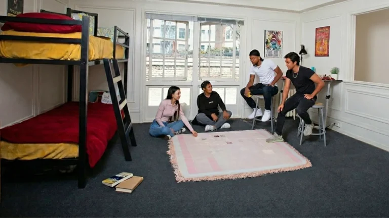 Four students sitting and talking on a rug in a university student housing room.