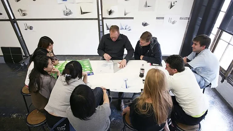 Group of nine people sitting around a table with a science demonstration, bottles, and a paper model.
