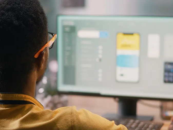 Person working on a smartphone app design at a computer monitor.