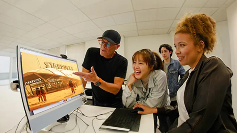 Group of four people gathered around a computer, looking at a design on a large monitor.