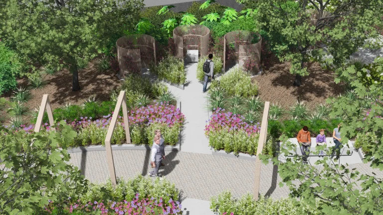 People walk along a garden path beside colorful flowers and tall green trees.
