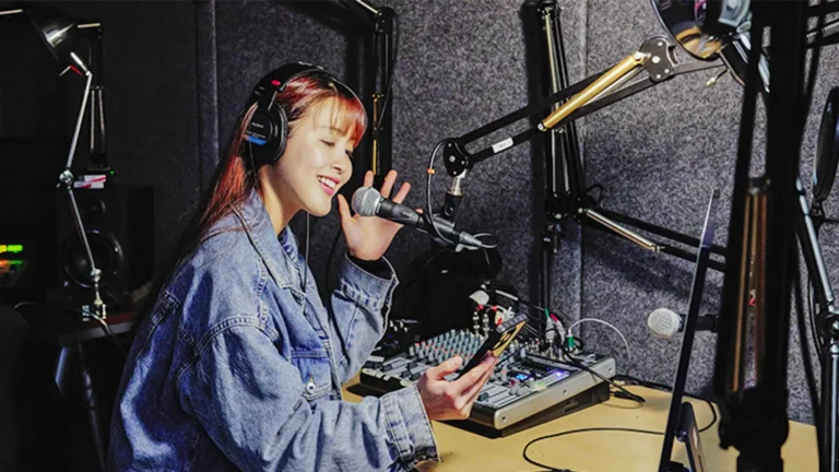 Female student in the Academy of Art University sound studio, wearing headphones and speaking into a microphone.