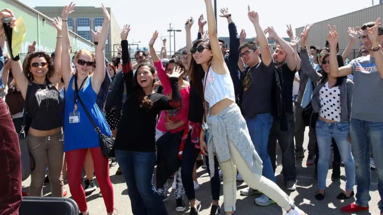 A diverse crowd of art students raise arms in celebration at an ArtU outdoor event.