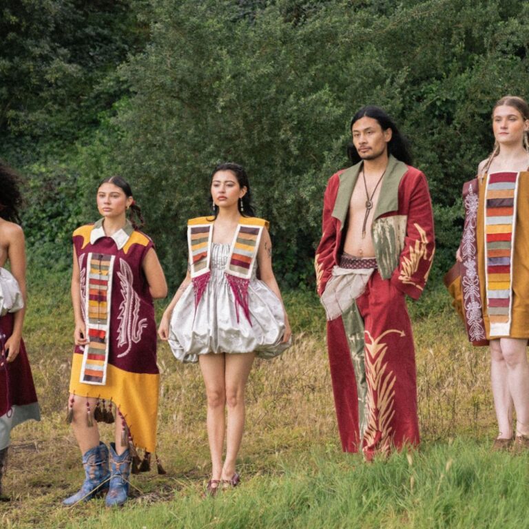 Group of people wearing colorful bohemian robes standing in a grassy field with trees.