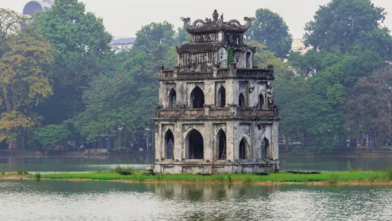Three-tiered ancient pagoda on a small island in a lake, surrounded by trees.