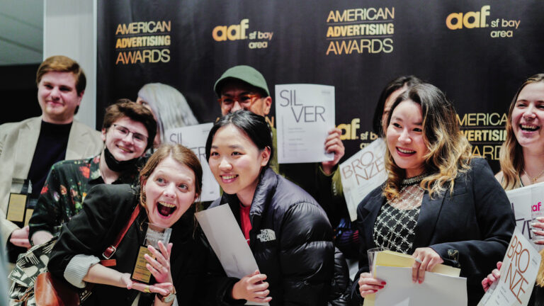 Group of smiling award finalists posing with certificates and papers at a backdrop event
