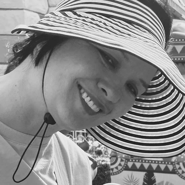 Smiling woman wearing a wide striped sun hat outdoors.