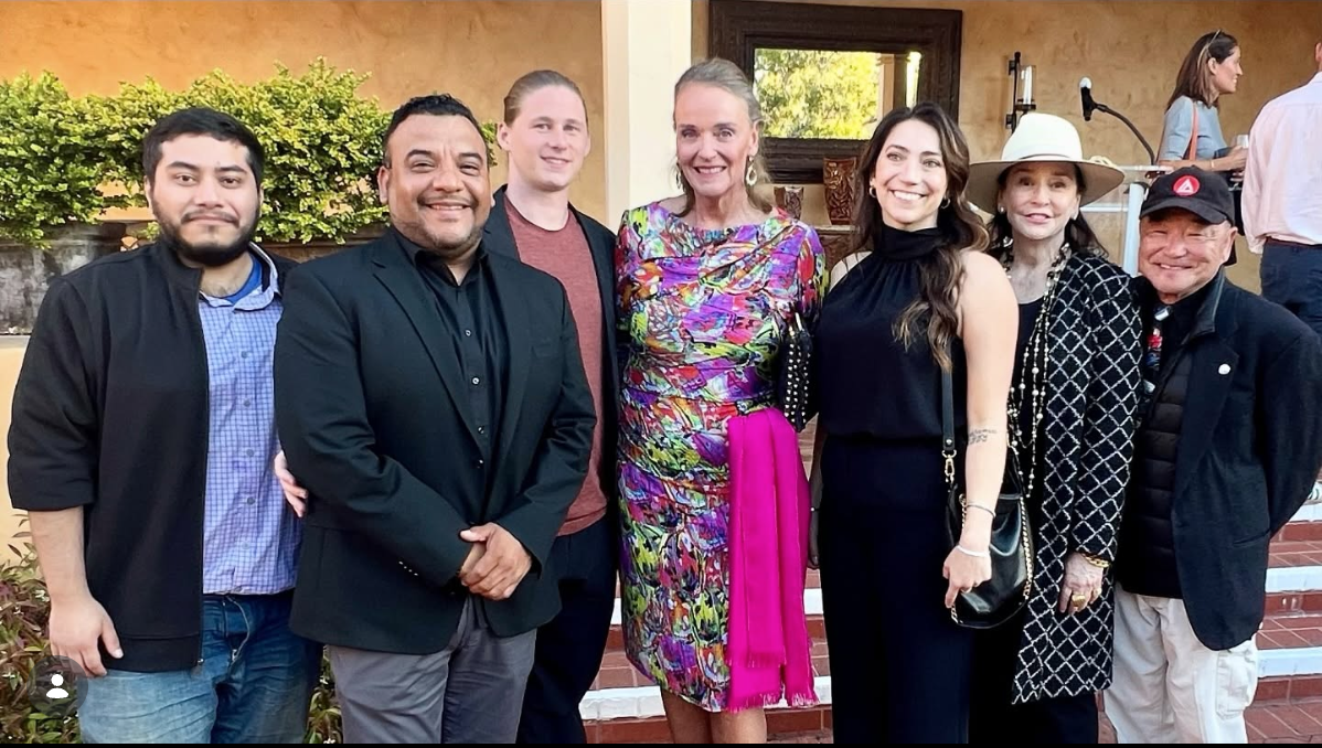 Group of seven people posing outdoors, smiling, dressed in semi-formal attire.