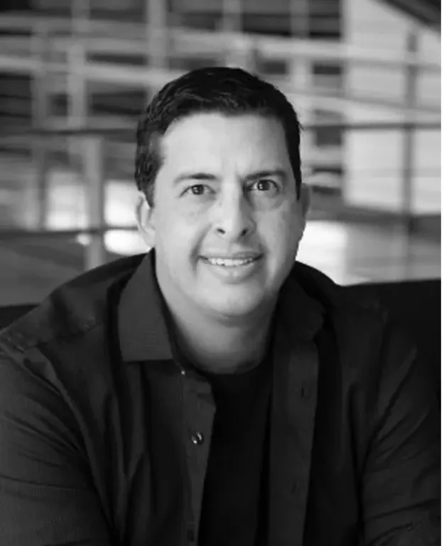 Smiling man in dark shirt in indoor setting with railings behind him