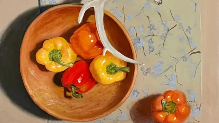 A wooden bowl holds vibrant bell peppers and a white antler, resting on a floral-patterned tablecloth. Another orange pepper sits nearby, enhancing the still life arrangement.