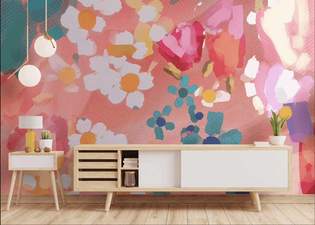 A wooden sideboard stands against a bright, floral-patterned wall. It holds a lamp, small plant, and decor items. Two pendant lights hang above, with a wooden floor beneath.