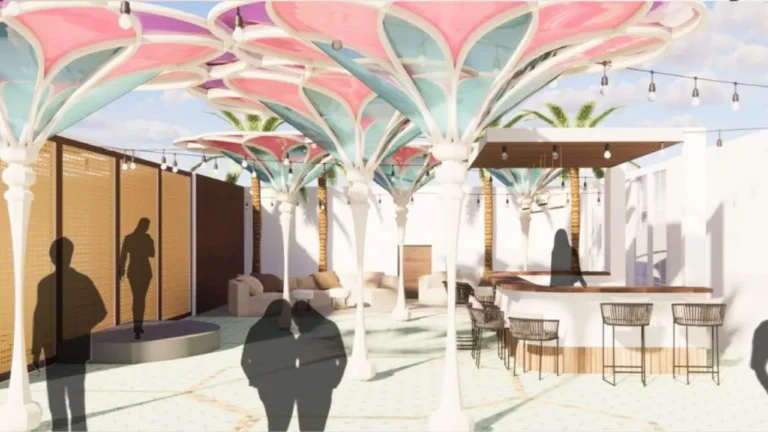 Colorful canopy structures create shade over an outdoor lounge area with seating, a wooden bar, and stools. Silhouettes of people are visible, with string lights overhead and palm trees nearby.
