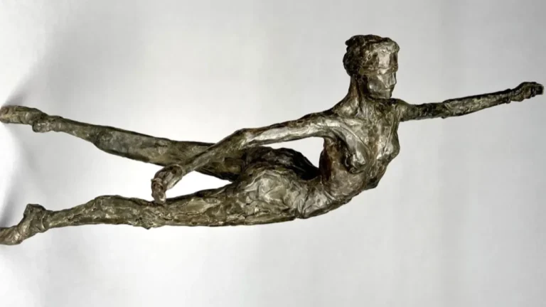 A bronze sculpture depicts a human form in a dynamic, horizontal flying pose with extended limbs, set against a plain white background.