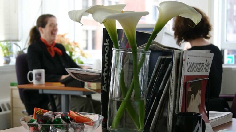 Vase holding white lilies stands on a table with magazines, including 