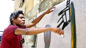 An individual paints on a large canvas, using a brush to create abstract shapes. They are outdoors, against a stone building. The scene captures a moment of artistic creation.